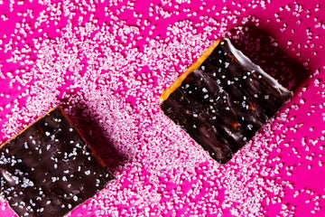 Two chocolate-covered caramel squares sprinkled with coarse sea salt on a bright magenta background