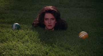 Woman's head emerging from a hole in grass between two striped balls